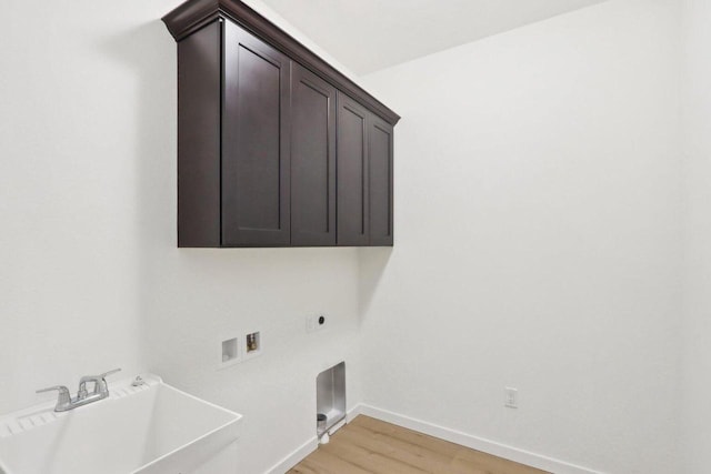 laundry room featuring light wood finished floors, cabinet space, a sink, electric dryer hookup, and baseboards