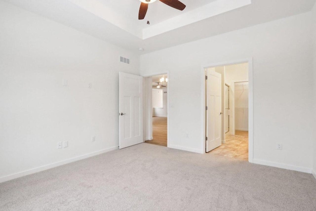 unfurnished bedroom with light carpet, a raised ceiling, visible vents, and baseboards