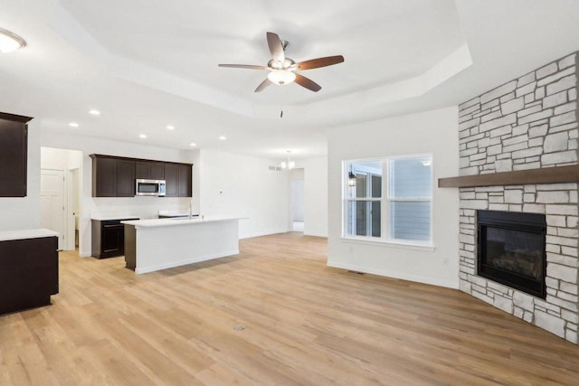 kitchen featuring a tray ceiling, stainless steel microwave, open floor plan, and light countertops