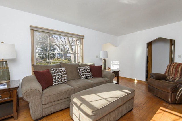 living area with arched walkways, light wood-style flooring, and baseboards