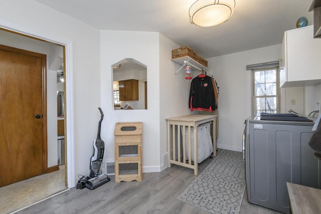 laundry room featuring washer / clothes dryer, arched walkways, cabinet space, light wood finished floors, and baseboards