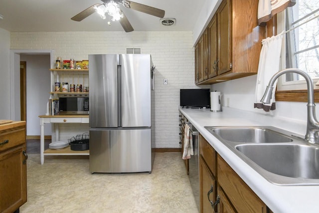 kitchen with brick wall, light countertops, appliances with stainless steel finishes, a ceiling fan, and a sink