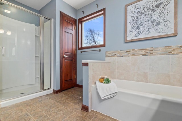 bathroom featuring a garden tub, a shower stall, and baseboards