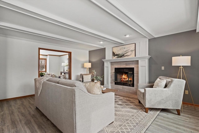 living area with a tiled fireplace, baseboards, beamed ceiling, and wood finished floors