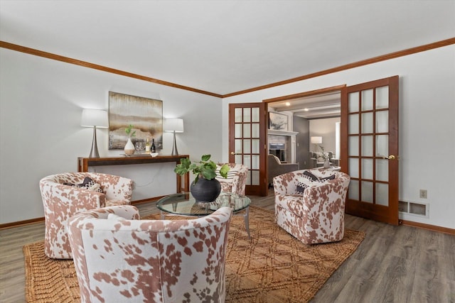 sitting room with a fireplace, wood finished floors, visible vents, baseboards, and ornamental molding