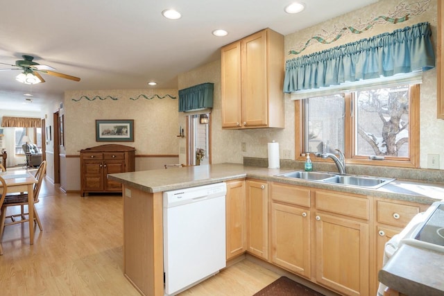 kitchen with a peninsula, white dishwasher, light wood-type flooring, light brown cabinets, and a sink