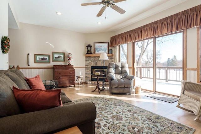 living room featuring recessed lighting, light wood-style floors, wainscoting, ceiling fan, and a stone fireplace