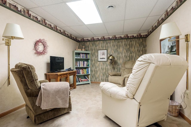 sitting room featuring wood walls, baseboards, and a drop ceiling