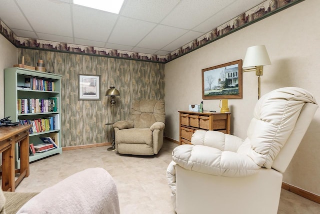 sitting room featuring a drop ceiling, wooden walls, and baseboards