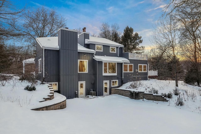 snow covered house featuring stairs, a chimney, and board and batten siding