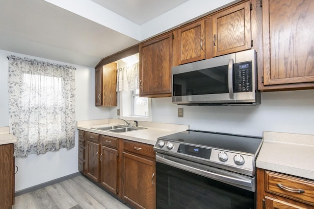 kitchen featuring stainless steel appliances, a sink, light countertops, brown cabinets, and light wood finished floors