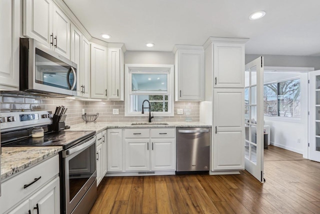 kitchen with dark wood-style floors, a sink, appliances with stainless steel finishes, white cabinetry, and tasteful backsplash