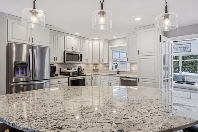 kitchen featuring light stone counters, a sink, decorative backsplash, appliances with stainless steel finishes, and white cabinetry