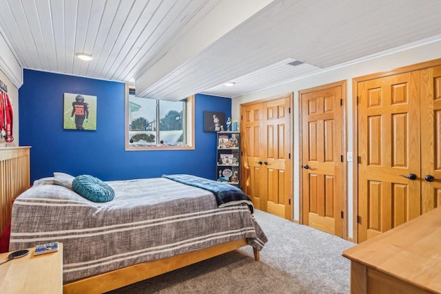 bedroom featuring carpet flooring, wooden ceiling, and multiple closets