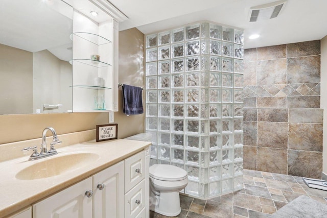 bathroom featuring vanity, visible vents, a walk in shower, stone finish flooring, and toilet