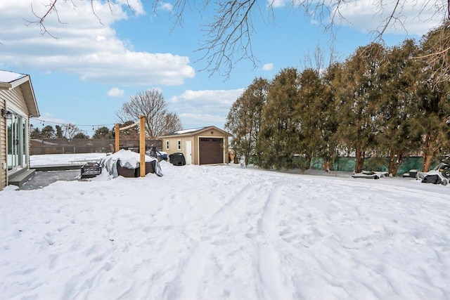 yard covered in snow with a detached garage, an outdoor structure, and fence