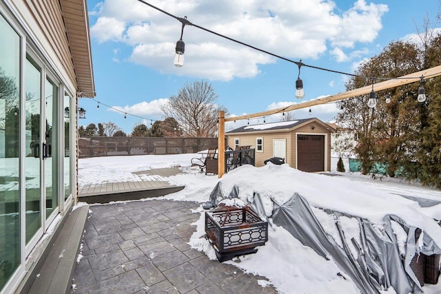 yard covered in snow with an outbuilding, fence, a detached garage, and a patio