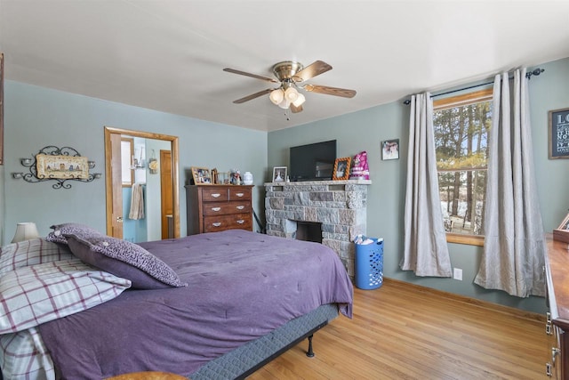 bedroom featuring a ceiling fan, a stone fireplace, and wood finished floors