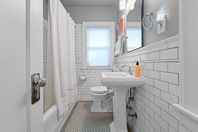 bathroom with tile walls, shower / bath combination with curtain, toilet, a sink, and tile patterned flooring