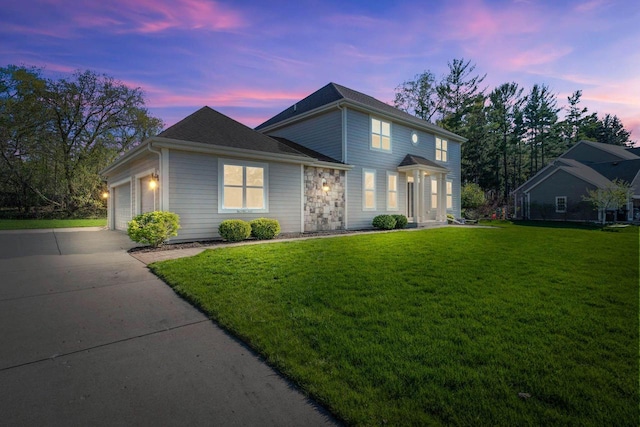 view of front facade featuring a yard, stone siding, driveway, and an attached garage