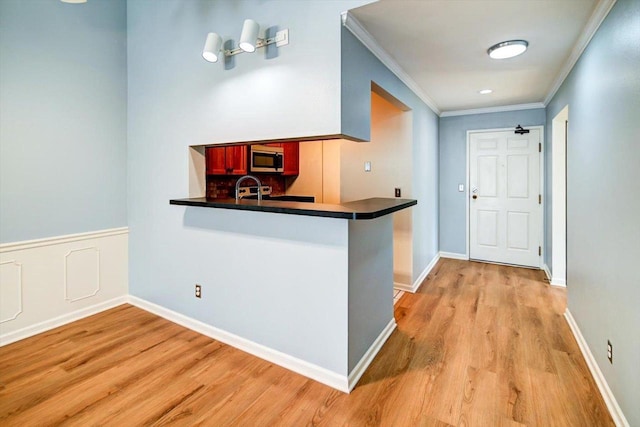 interior space with dark countertops, stainless steel microwave, light wood-style flooring, ornamental molding, and a peninsula