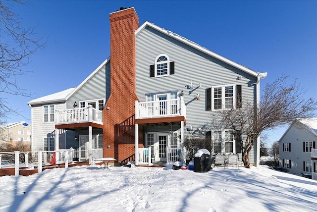 snow covered property with a chimney and a balcony