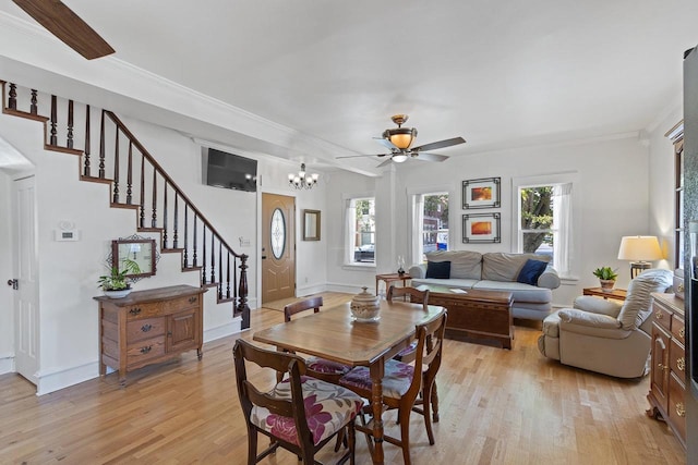 dining space with light wood-style flooring, ceiling fan with notable chandelier, baseboards, ornamental molding, and stairway