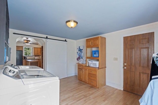 laundry area with laundry area, a barn door, crown molding, light wood-type flooring, and washing machine and dryer