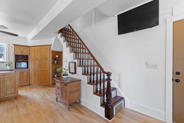 stairway featuring baseboards, wood finished floors, a ceiling fan, and crown molding