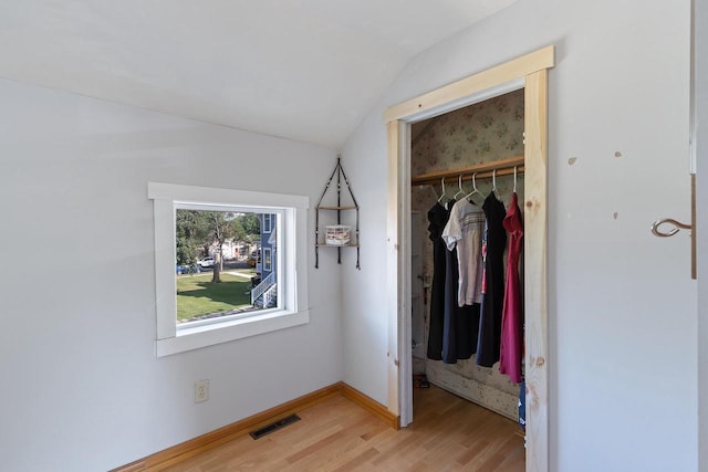 unfurnished bedroom featuring baseboards, visible vents, light wood-style flooring, vaulted ceiling, and a closet