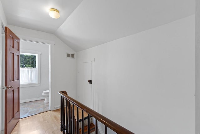 corridor with baseboards, visible vents, vaulted ceiling, an upstairs landing, and light wood-style floors