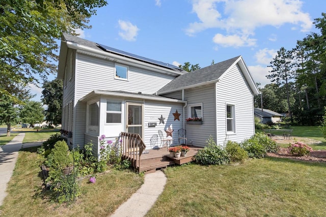 view of front facade with a front yard, a wooden deck, and roof mounted solar panels