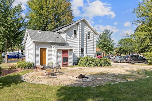 back of house with an outdoor fire pit, a lawn, and roof with shingles