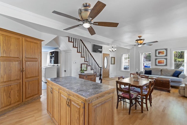 kitchen with light wood finished floors, dark countertops, a kitchen island, open floor plan, and crown molding