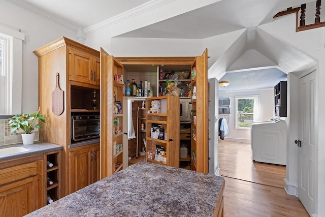 kitchen featuring light wood-style floors, brown cabinetry, crown molding, and a sink