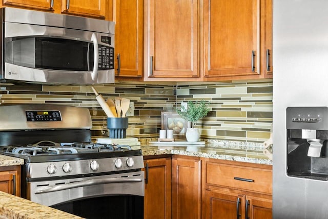 kitchen featuring stainless steel appliances, brown cabinets, light stone counters, and tasteful backsplash