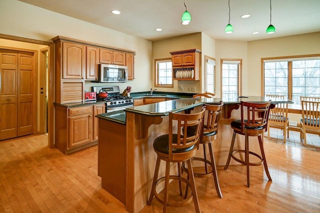 kitchen with brown cabinets, dark countertops, hanging light fixtures, appliances with stainless steel finishes, and a kitchen island