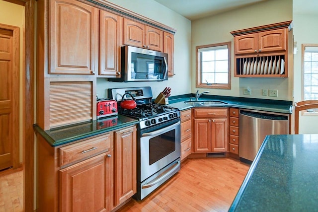 kitchen featuring light wood-style flooring, a sink, appliances with stainless steel finishes, brown cabinetry, and dark countertops