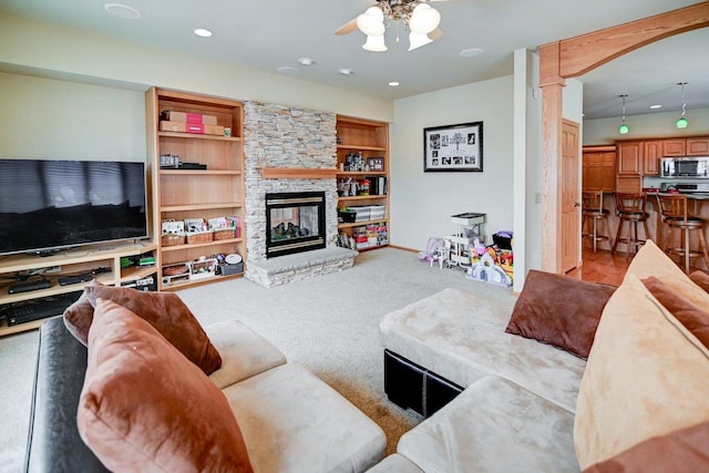 living area with built in features, recessed lighting, light colored carpet, ceiling fan, and a stone fireplace