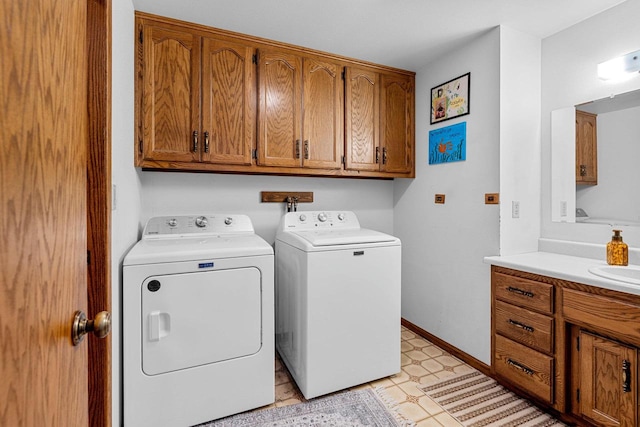 laundry area featuring cabinet space, baseboards, washer and clothes dryer, light floors, and a sink