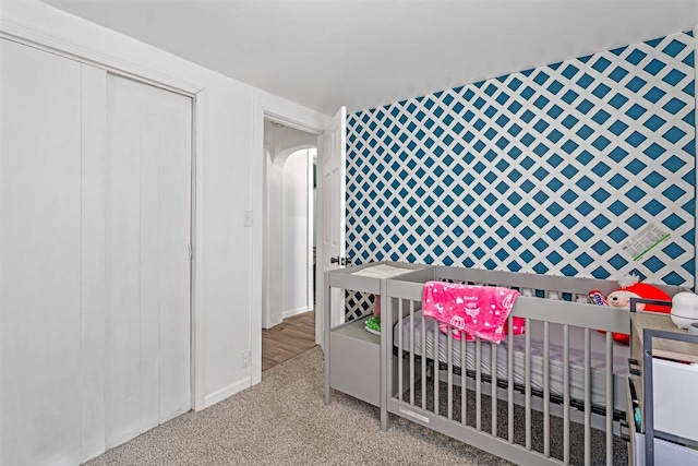 carpeted bedroom featuring a nursery area and an accent wall