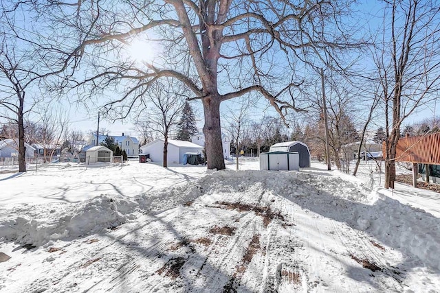 snowy yard with a garage, a residential view, a storage unit, and an outdoor structure