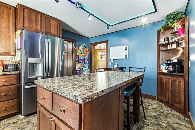 kitchen with open shelves, a kitchen island, a kitchen breakfast bar, stone finish flooring, and stainless steel fridge