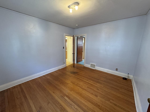 spare room featuring wood finished floors, visible vents, and baseboards