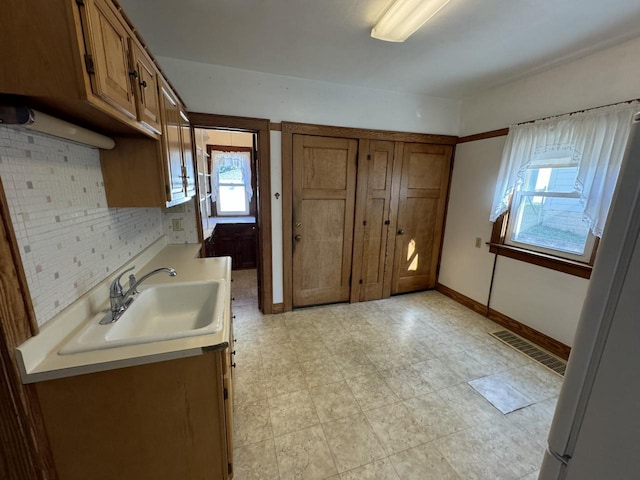 kitchen with a sink, visible vents, light countertops, brown cabinets, and decorative backsplash