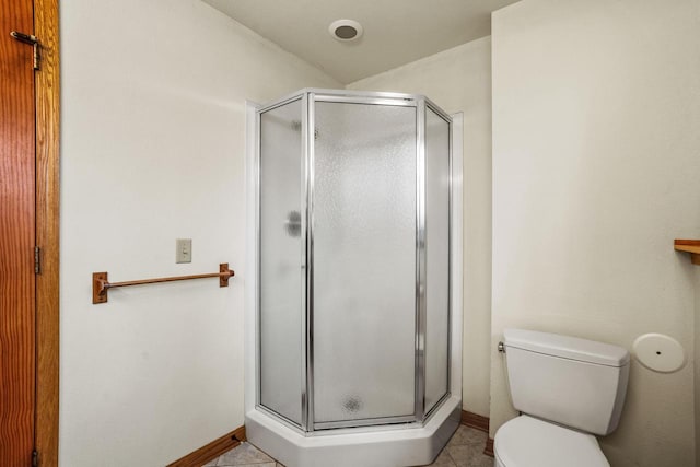 bathroom featuring toilet, a stall shower, tile patterned flooring, and baseboards