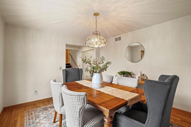 dining room featuring wood finished floors, visible vents, baseboards, stairway, and an inviting chandelier