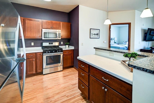 kitchen featuring light wood finished floors, appliances with stainless steel finishes, brown cabinetry, and decorative light fixtures