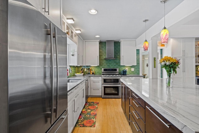 kitchen featuring tasteful backsplash, white cabinets, decorative light fixtures, stainless steel appliances, and wall chimney range hood