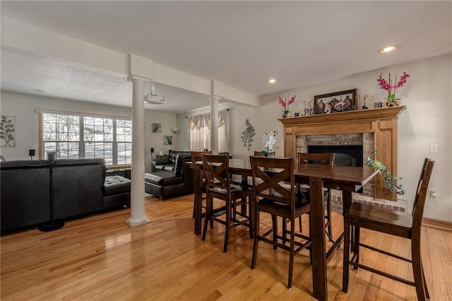 dining room with light wood-style floors, recessed lighting, a brick fireplace, and decorative columns